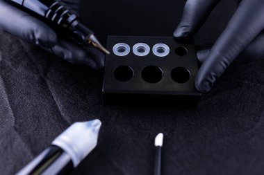 Kalıcı kaş makyajcısının eline yakın plan. Dövme makinesinin kartuşunda pigment kazanıyor.