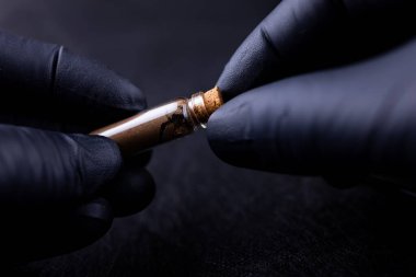 Siyah eldivenli bir usta kaş boyama için bir şişe kına tutuyor.