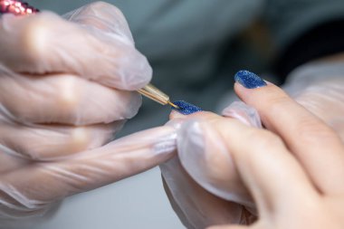 Manikür ustası yakın plan, tırnak fırçasının yüzeyine ince bir oje sürerek dağıtılır.