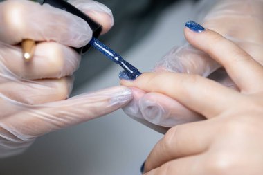 Manikür ustası, jöle cilasının son katmanını müşterinin tırnağına uyguluyor.