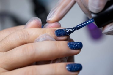 Manikür ustası, tırnak yüzeyine jöle sürmenin son aşamasını bir fırçayla gerçekleştirir.
