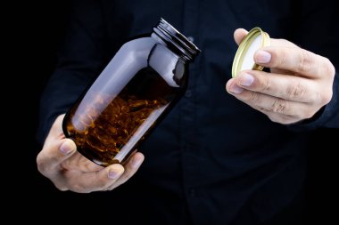 in the hands of a man, a jar with fish oil capsules, he unscrews the lid