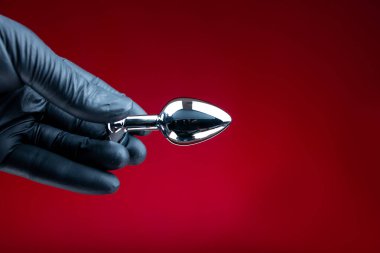 Erotik bdsm oyunları için gümüş anal fiş tutan siyah eldivenli eller.