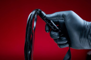 Erotik bdsm oyunları için siyah eldivenli eller deri kamçı tutuyor.