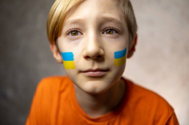 Savaşa karşı bir çocuk, yanaklarında Ukrayna bayrağı olan düşünceli bir çocuk yukarı bakar ve dünya barışını hayal eder.