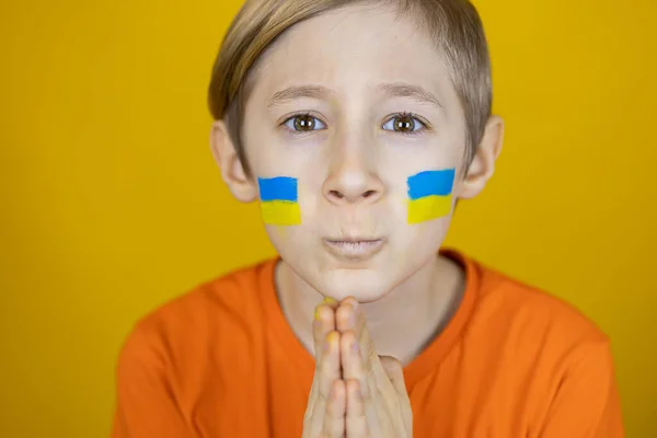 Smutny Chłopiec Namalowaną Flagą Ukrainy Policzkach Złożył Dłonie Przed Twarzą — Zdjęcie stockowe