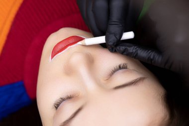 Ustası dövmesini yaptırmadan önce dudaklarında beyaz kalemle iz bırakan bir kız için kalıcı dudak dövmesi prosedürü.