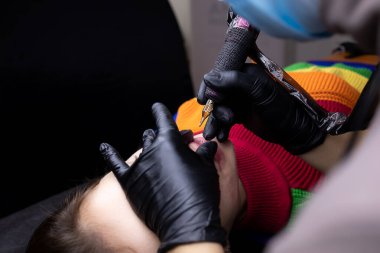 Kozmetoloji ofisinde, kalıcı makyaj ustası dudak dövmesini tek eliyle yapar.