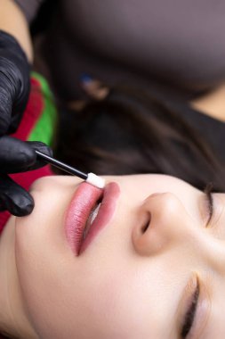 Siyah eldivenli usta, daimi dudak dövmesi işleminden sonra modelin dudaklarında fırça yağı ile uygulanır.