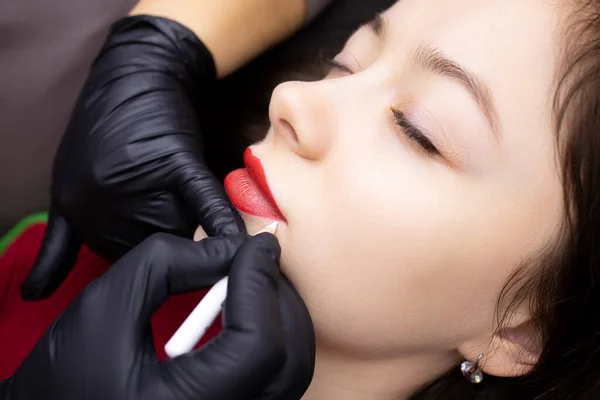 the procedure of permanent lip tattooing master in black gloves outlines the contour of the lips with a white pencil