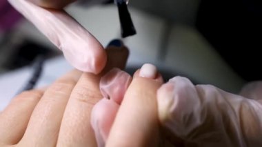 Manikür ve pedikür ustası siyah bir fırçayla beyaz oje sür.