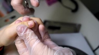 Manikürcü ve pedikür uzmanı çocuğun tırnaklarını makasla kesiyor.