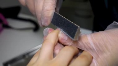 Manikür ve pedikür ustası bir çocuğun tırnaklarını tırnak törpüsüyle ezer.