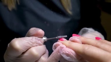 Manikür ve pedikür ustası manikür makinesi ile eski tırnak cilasını çıkartıyor.