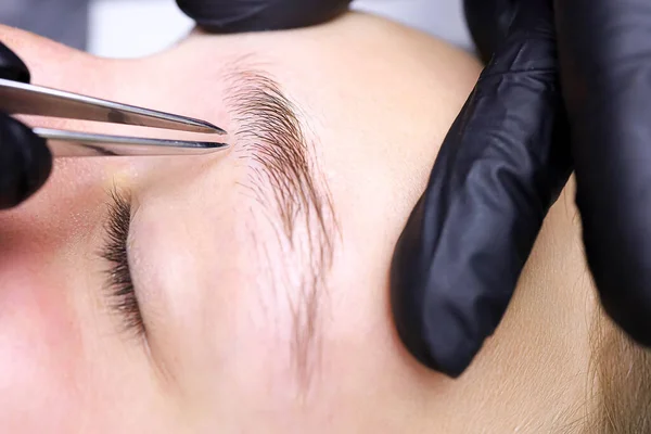 plucking unwanted eyebrow hairs after laminating the eyebrows with tweezers