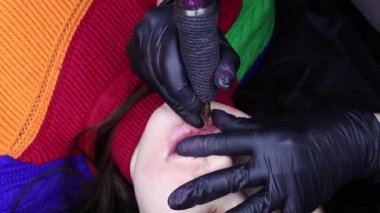 Üst görünüm dudak kalıcı makyaj prosedürü ustası modelin dudağını tutuyor ve makineyi kullanarak dövme yapıyor