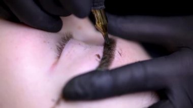 Kalıcı kaş makyajı prosedürü ustası kaşlarını esnetir ve kaşlarını dövme yapar.