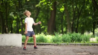 Parkta beyaz tişörtlü bir çocuk topu duvara fırlatıyor.