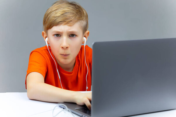 a child sits at a laptop with headphones in his ears and listens to music, typing on a computer