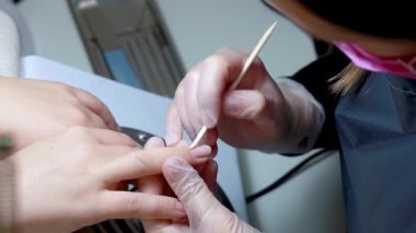 Manikür ustası odun sopayla tırnak etlerini temizler.