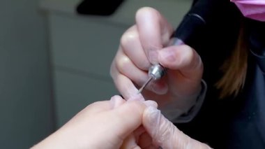 Manikür ustası, müşterinin parmağını tutarak tırnak törpüsü makinesiyle tüm çiviyi çözüyor.