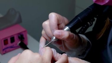 Bir makinenin yardımıyla manikür çivinin yakınındaki fazla deriyi temizler.