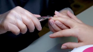 Manikür ustasının ellerinin yakın çekimi tırnak makasını tutarak derinin fazlalığını azaltır.
