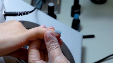 Manikür ustası mavi tırnak cilası sürmüş. Müşterinin tırnağı onu parmağından tutmuş.