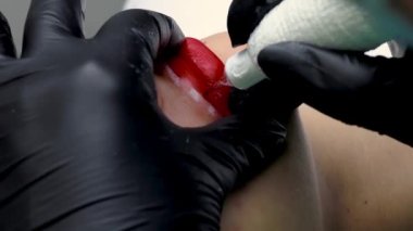 Ustanın kalıcı dudak makyajı prosedürüne yakın plan bir dövme makinesi kullanarak kırmızı dudaklarına dövme uygular.