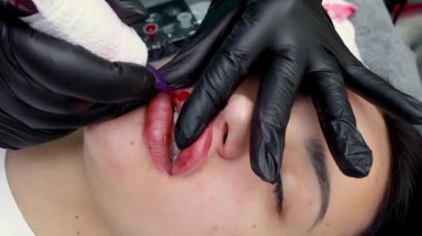 Bir dövme makinesi ve kırmızı pigmentle kalıcı dudak makyajı yapan model bir kızın dudaklarının yakın çekimi.