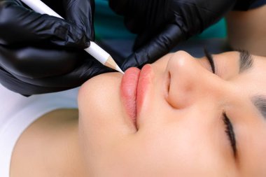 Dudakların kalıcı makyajından önce, modelin dudaklarını kapatıyoruz, usta dudaklara beyaz bir kalemle işaret koyuyor.