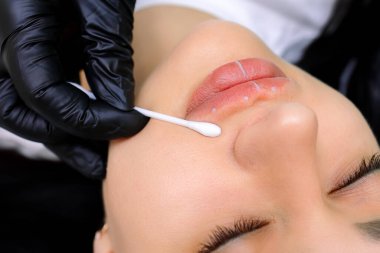 Kalıcı dudak makyajı işleminden önce, usta izleri pamuklu bezle siler.
