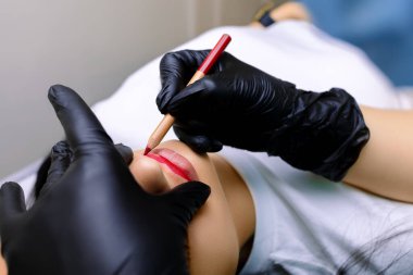 Siyah eldivenli kalıcı makyaj ustası dudak tutar ve dövme yapmak için kırmızı kalemle boyar.