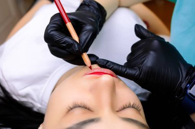 Modelin dudaklarına yakın çekim, üstat kalıcı makyaj için kırmızı kalemle boyuyor.