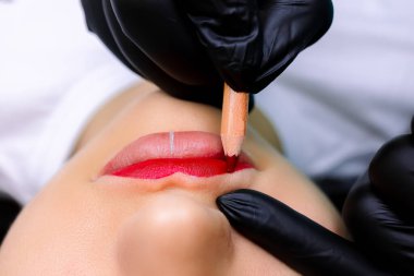 Modelin dudaklarına yakın çekim, üstat kalıcı makyaj için kırmızı kalemle boyuyor.