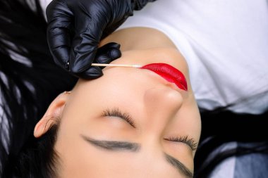 Dövme işleminden önce dudaklarındaki fazla kırmızı ruju pamuklu çubukla temizleyen kalıcı bir makyaj ustasının eli.