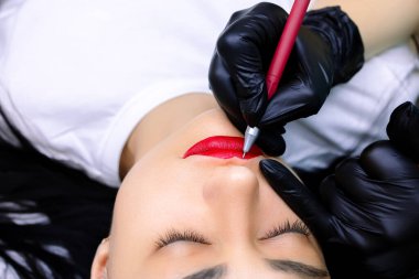 Dövme ustası, mankenin dudaklarına bir kalem çizer.