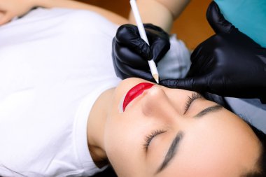 Dudakların kalıcı makyajından önce, usta zaten yapılmış olan dudakları yuvarlak içine alır ve çevreye beyaz bir çizgi çizer.