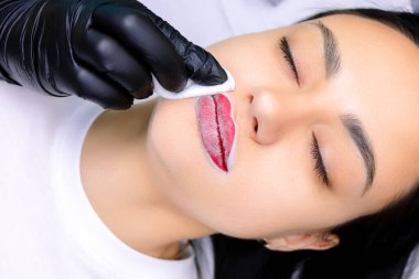 Usta önceden hazırlanmış ve kırmızı boyanmış dudaklara dövme prosedüründen önce pudra sürüyor.