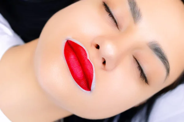 Bir modelin dudaklarının makro fotoğrafçılığı kalıcı bir makyaj prosedürü için hazırlanır ve kırmızı onlara uygulanır.