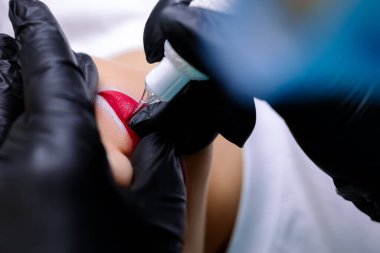 Bir daktiloyla çalışarak ve dudaklarına dövme uygulayarak dudak dövmesi yapan kalıcı bir makyaj sanatçısının elleri.