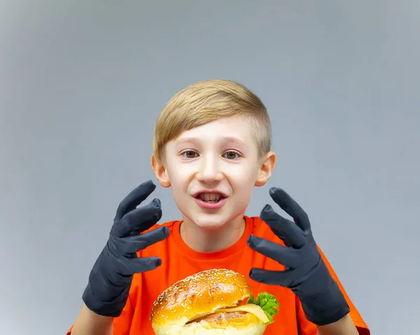 Zaskoczony Chłopiec Siedzi Przed Wielkim Burgerem Pokazuje Ręce Czarnych Rękawiczkach — Zdjęcie stockowe