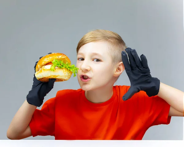 Der Junge Hält Einen Burger Vor Sich Hat Schwarze Handschuhe — Stockfoto