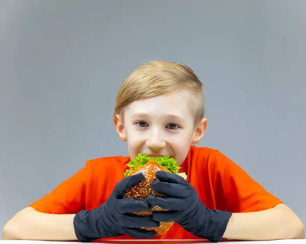 Neşeli Bir Çocuk Masada Oturur Önünde Sulu Bir Burger Tutar — Stok fotoğraf