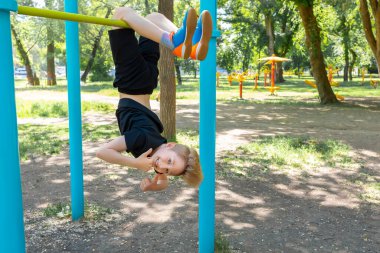 Sporcu çocuk baş aşağı sarkıyor ve gülüyor.