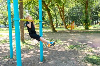 Sporcu çocuk kendini çenesine kadar yukarı çekti ve parkta jimnastik egzersizleri yaptı.