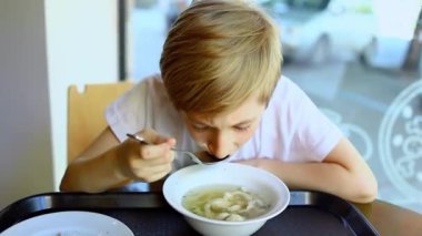 Restoranda bir çocuk çorba içer ve pencereden dışarı bakar.