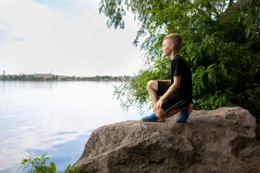Gezgin çocuk büyük bir taşın üzerinde duran nehre bakıyor.