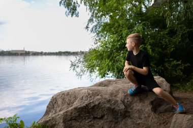 Çocuk nehre bakmak için taşın kenarına git.