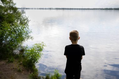 Çocuk arkasını dönüp nehre bakıyor.